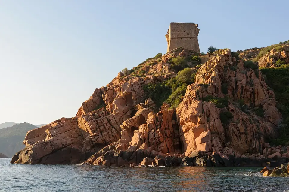 Tour génoise carrée au sommet d'un promontoire de roche rouge plongeant dans la mer, à Porto